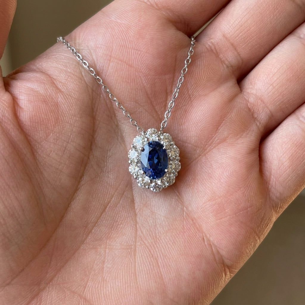 Close-up held in hand, 0.8ct oval blue sapphire pendant necklace featuring halo setting.