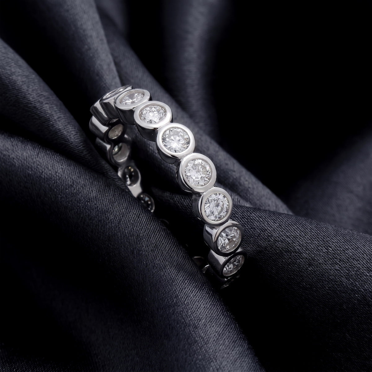 Angled view showing bezel setting of 1.31 ctw round lab grown diamond eternity ring on black silk   