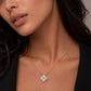 A close-up of a woman wearing a delicate gold chain necklace with a small four-petal flower pendant set with clear stones, styled with a black top.