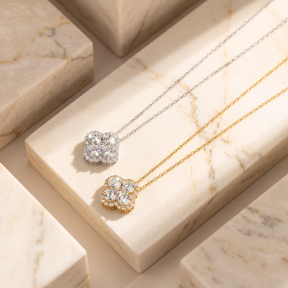 Two floral cluster pendant necklaces displayed on cream marble blocks. One pendant is silver-toned with clear stones, and the other is gold-toned with clear stones, set against a warm beige marble background.