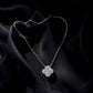 A silver-toned necklace with a four-petal flower pendant, set against a draped black satin fabric background.