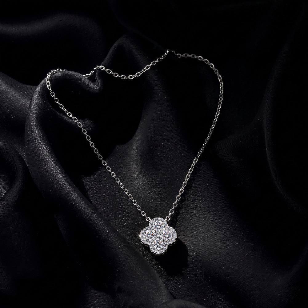 A silver-toned necklace with a four-petal flower pendant, set against a draped black satin fabric background.