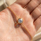 A gold chain bracelet with a round bezel-set iridescent gemstone, shown resting on an open hand in bright sunlight.
