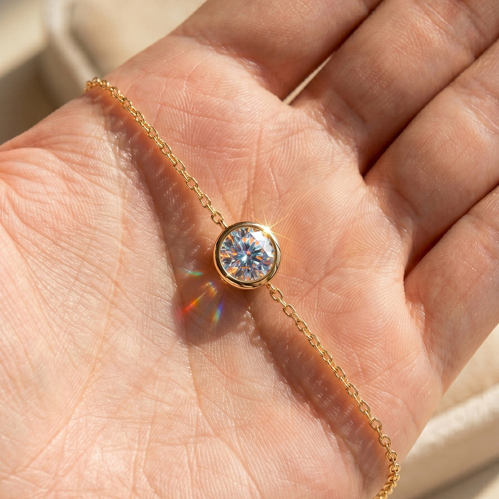 A gold chain bracelet with a round bezel-set iridescent gemstone, shown resting on an open hand in bright sunlight.