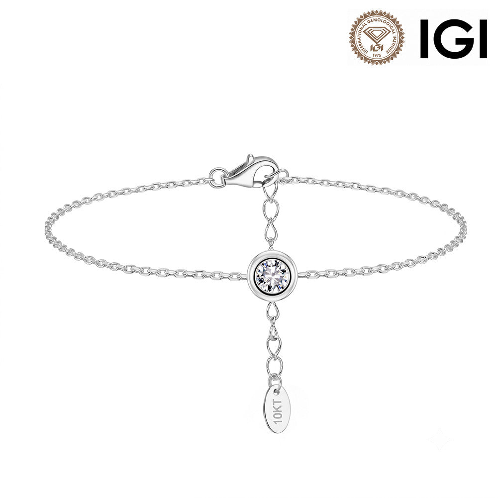 A silver chain bracelet with a round bezel-set clear gemstone and a dangling heart-shaped charm engraved with 'IGI', shown on a white background with an IGI logo in the top right corner.