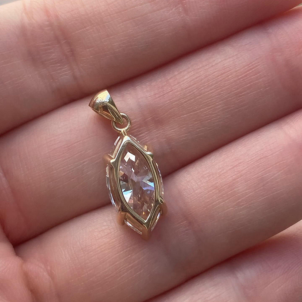A gold pendant with a marquise-cut clear gemstone resting on a person's fingers.