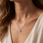 A close-up of a woman's neck and chest wearing a delicate gold chain necklace with a small heart-shaped clear gemstone pendant.