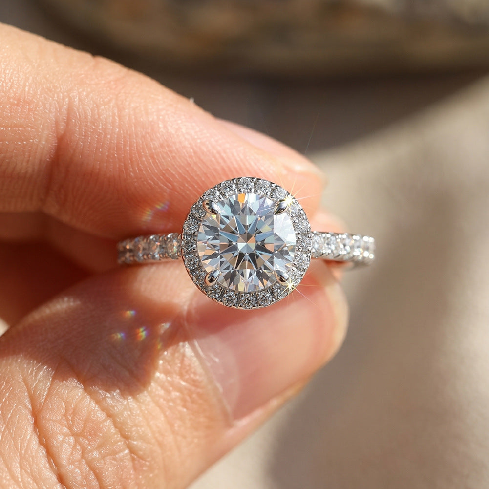 Hand holding 10k white gold round brilliant lab diamond halo ring with pave accents in daylight