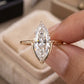 Hand holding 14k yellow gold marquise cut lab diamond solitaire V ring above beige velvet box