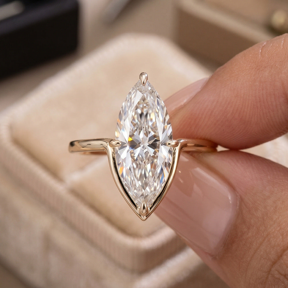 Hand holding 14k yellow gold marquise cut lab diamond solitaire V ring above beige velvet box