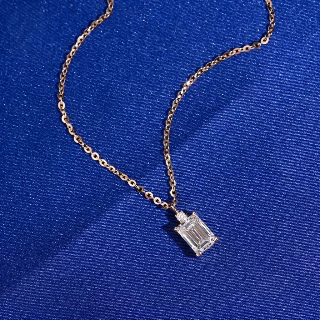 Angle view of 18k rose gold 1 carat radiant cut lab-grown diamond clavicle pendant necklace on blue fabric
