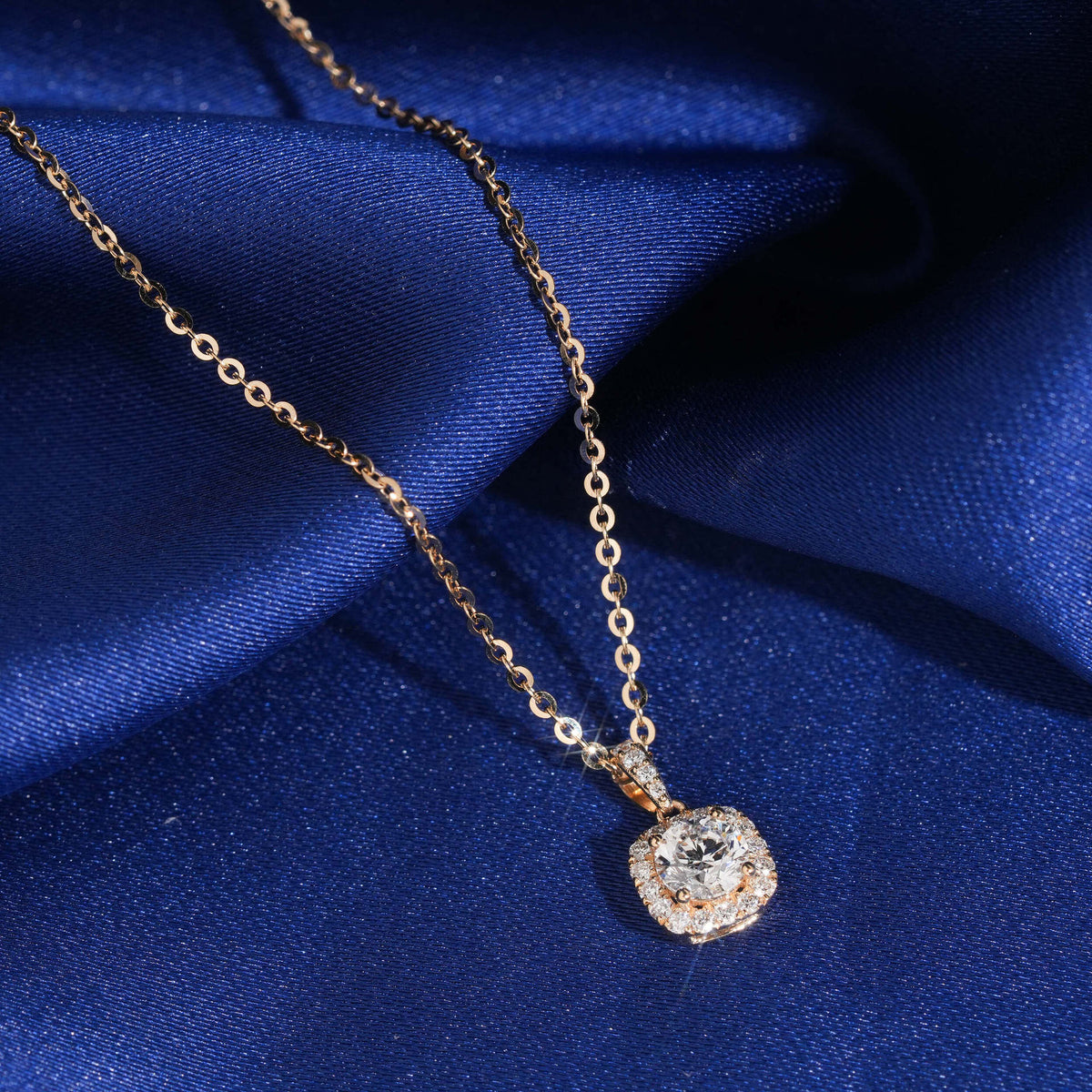 Angle view of 18k rose gold 5mm cushion square halo lab-grown diamond pendant necklace on blue fabric