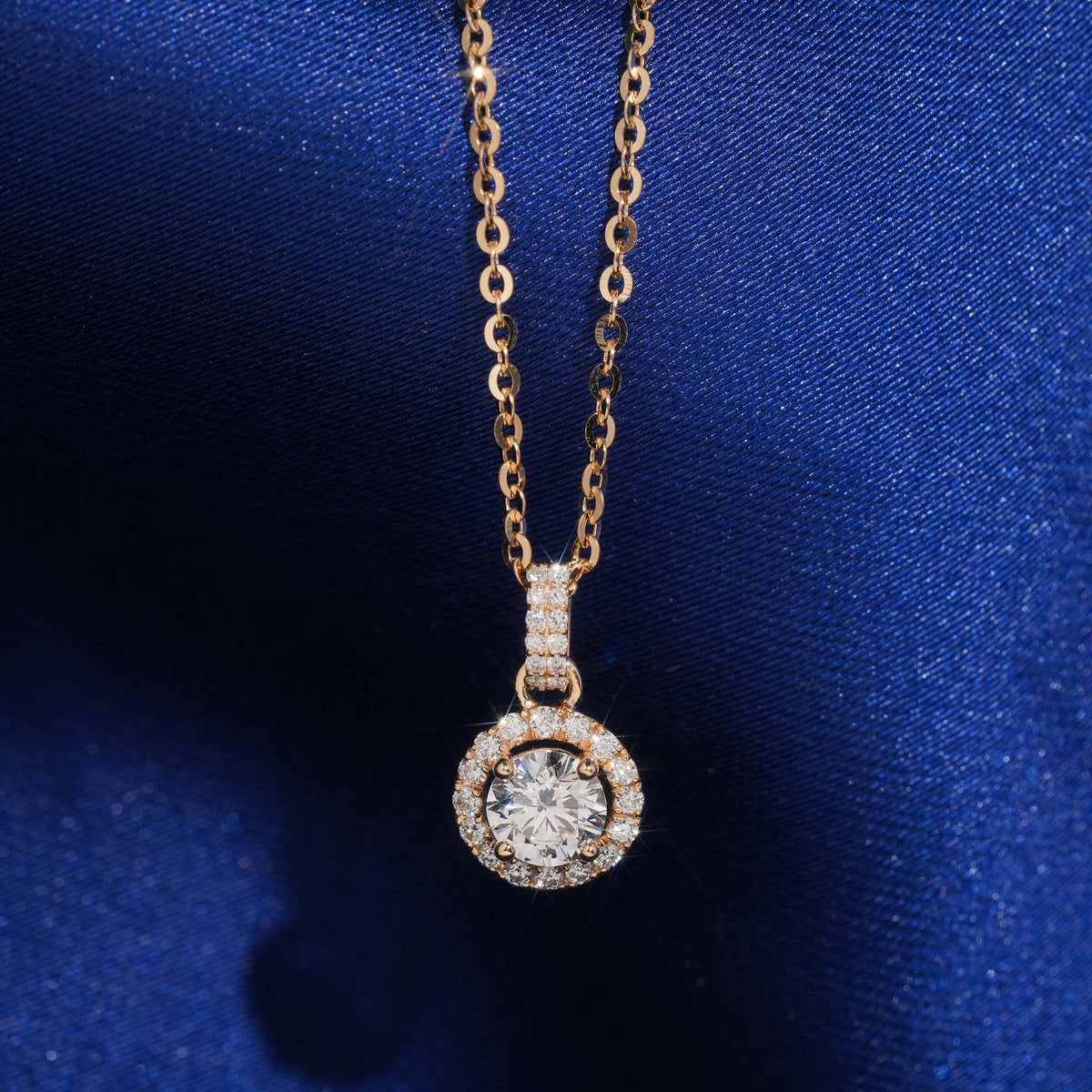 18k rose gold 5mm round halo lab-grown diamond clavicle pendant necklace on royal blue silk background   