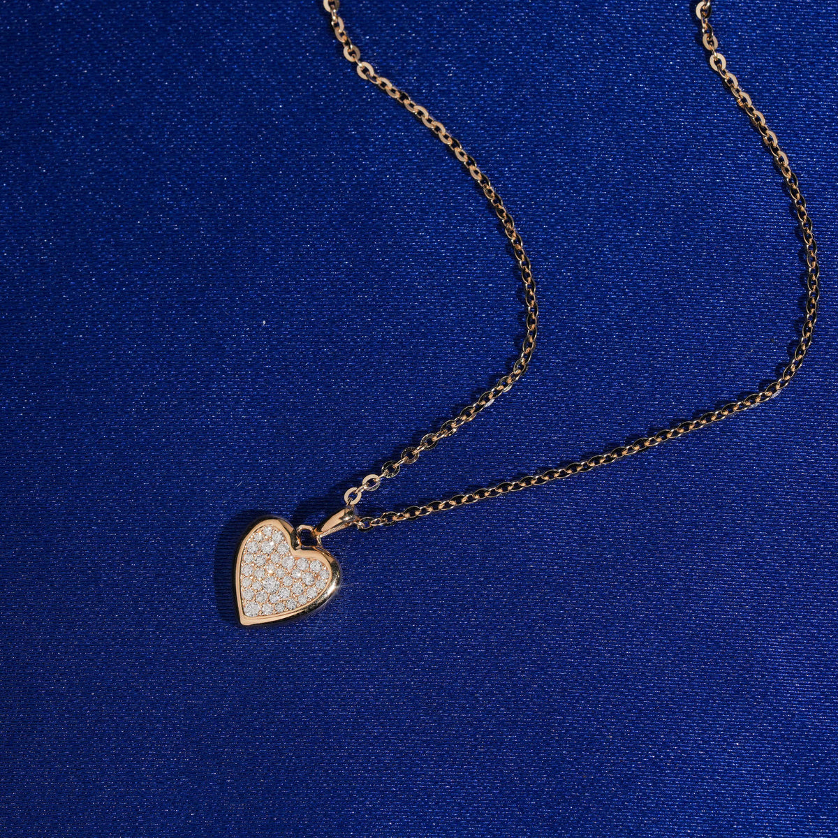 Angle view of 18k rose gold pave lab-grown diamond heart pendant necklace on blue fabric