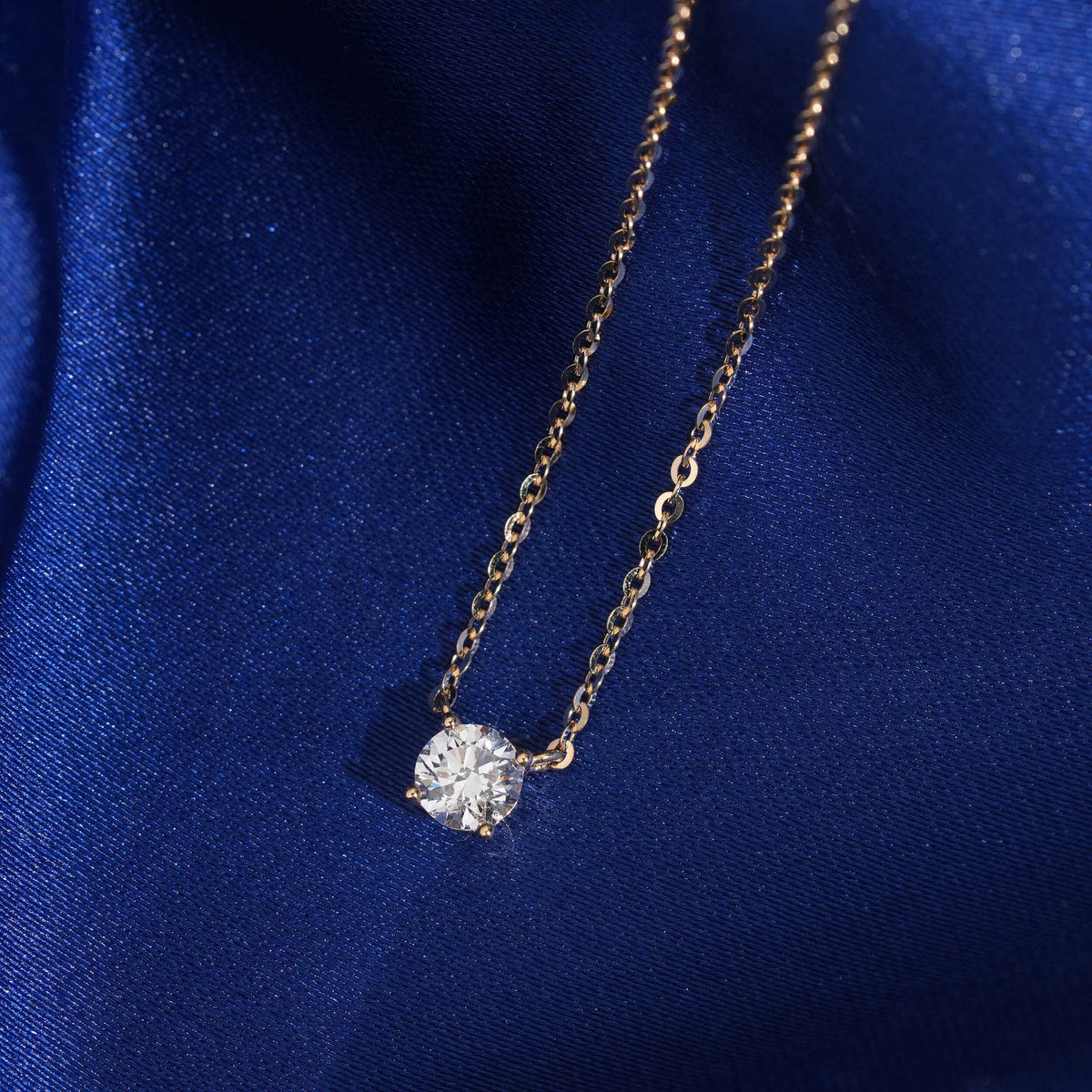 Close up view of 5.5mm round solitaire lab-grown diamond in 18k yellow gold setting on blue silk