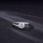 1ct round diamond bypass solitaire ring lying flat on dark grey background.