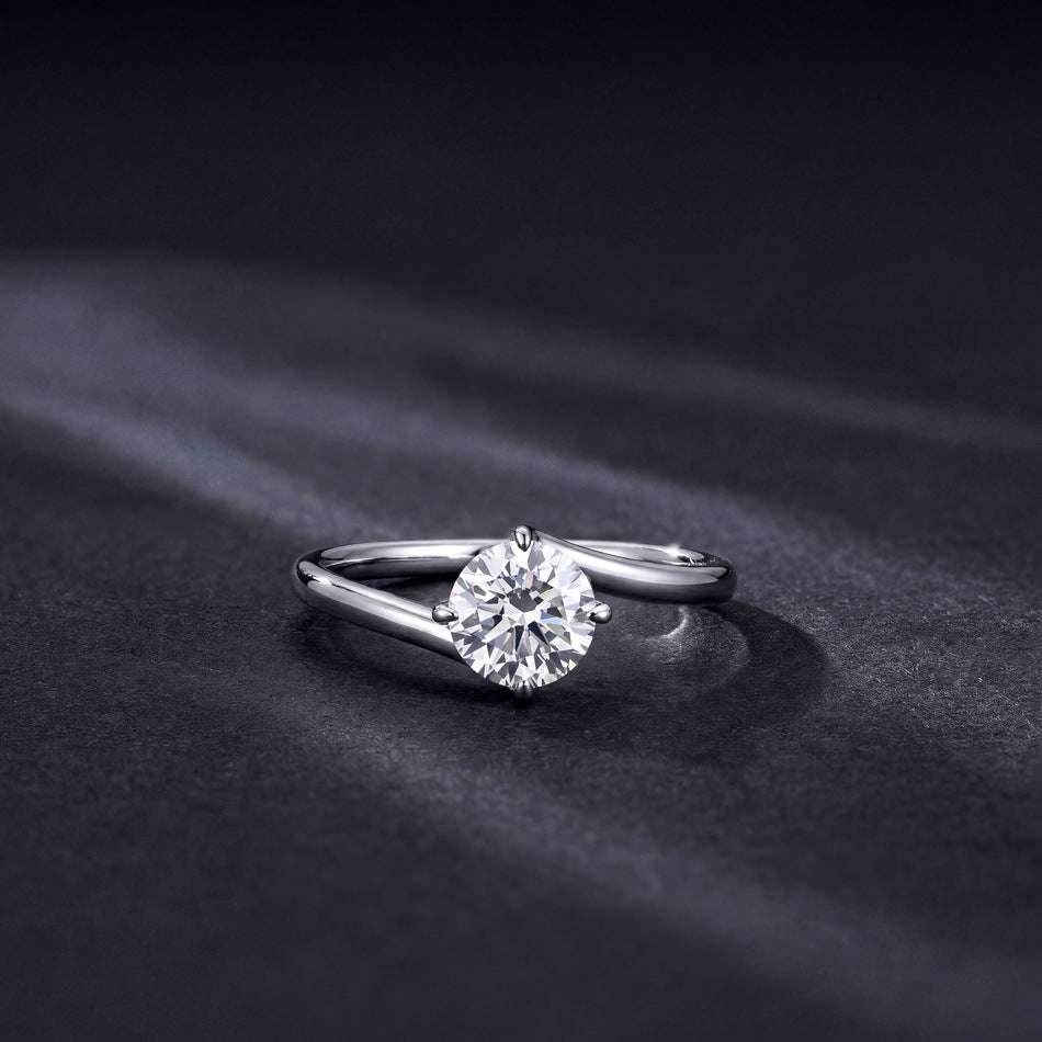 1ct round diamond bypass solitaire ring lying flat on dark grey background.