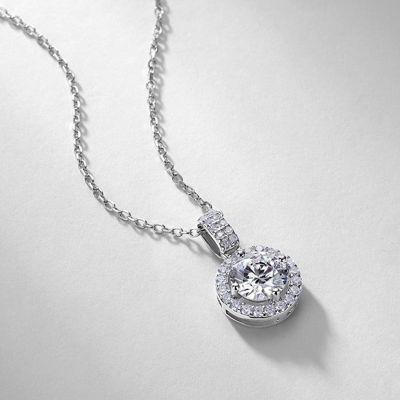Perspective view of 1ct round halo diamond pendant resting on light surface.