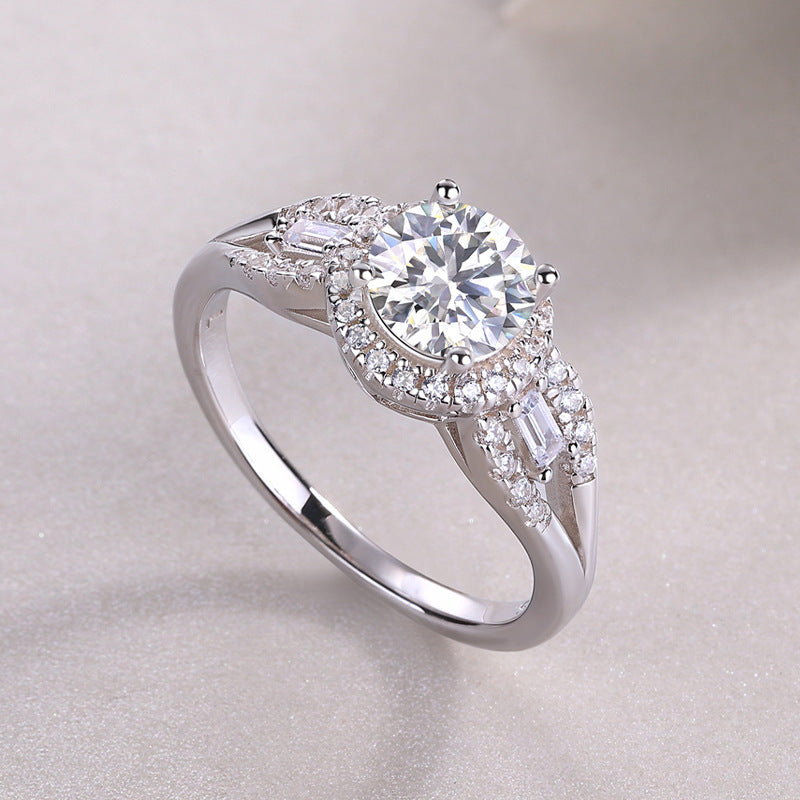 Silver 1CT round moissanite halo ring with baguette side accents resting on a soft background.