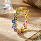 Gold 2.5mm princess cut rainbow gradient gemstone eternity band ring on travertine stone surface