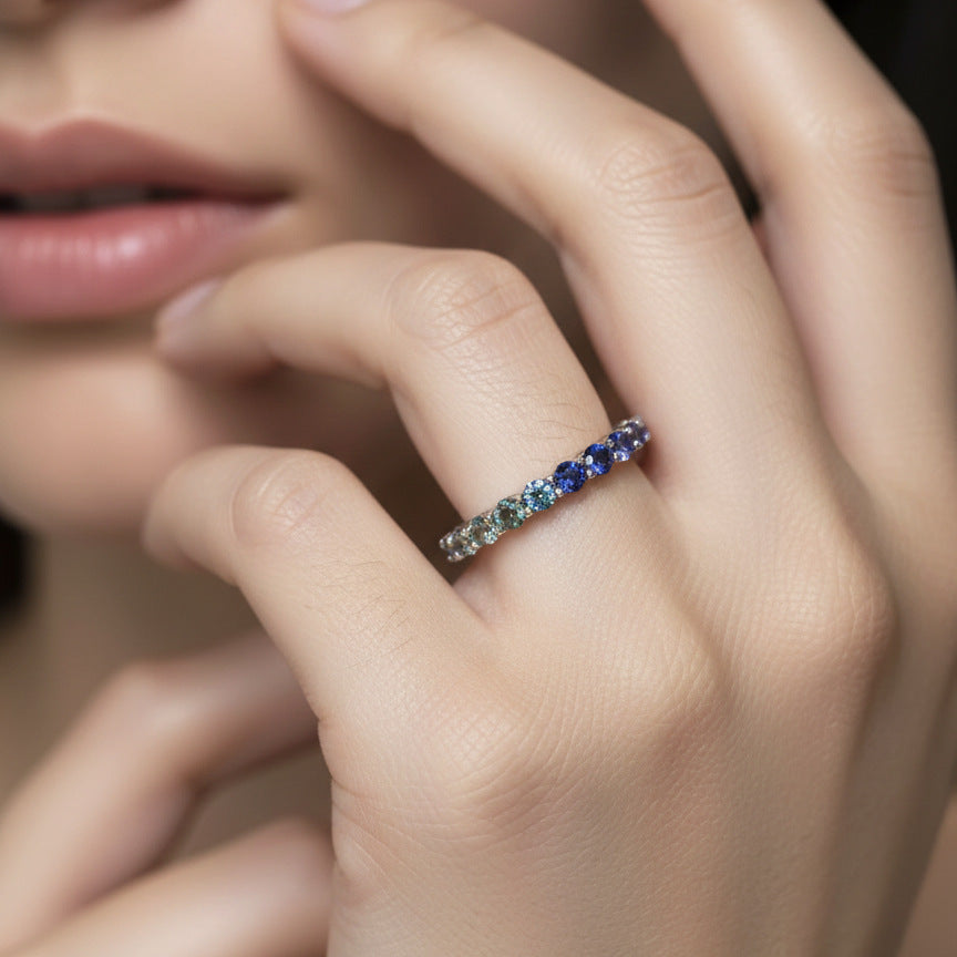 Model wearing gold 2.5mm round rainbow gradient gemstone eternity band ring on finger