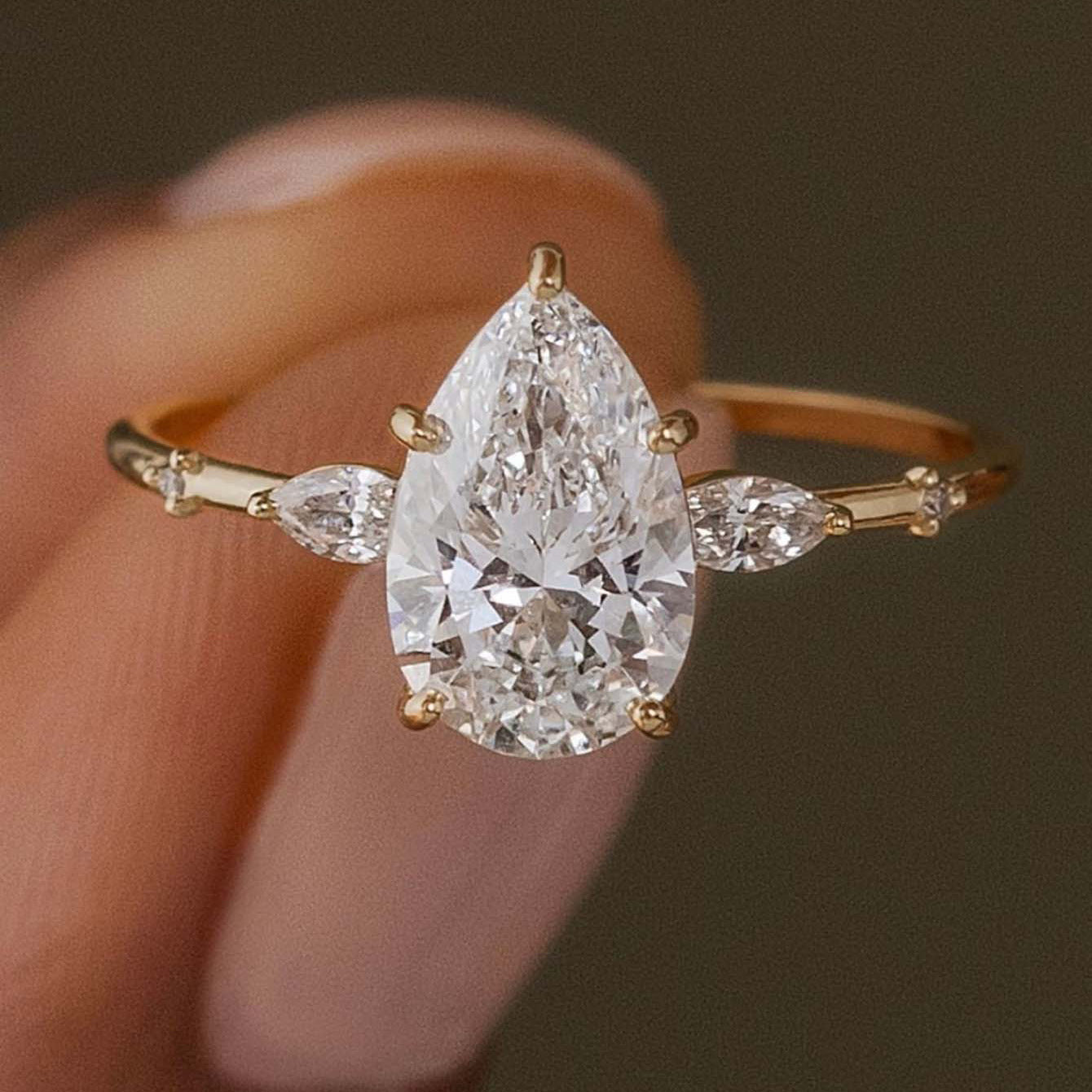  Yellow gold petal teardrop ring on soft romantic background. Alt: “2CT Petal-Shaped Teardrop Moissanite Ring – 18K Yellow Gold.”