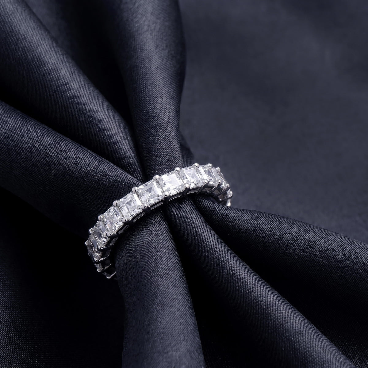 Angled view showing prong setting of 3.88 ctw asscher cut lab grown diamond eternity ring on black silk