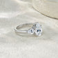 Silver 3CT pear moissanite three-stone ring resting on a light textured background.