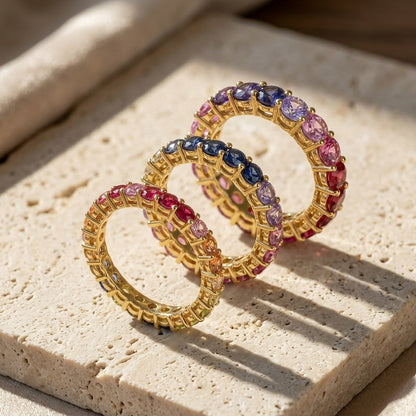 Gold 3mm 4mm and 5mm round rainbow gradient moissanite eternity band rings compared on travertine stone