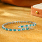 Angled view of 3.0mm lab grown paraiba tourmaline and moissanite tennis bracelet on warm suede surface   