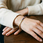 Model wearing gold 3mm round rainbow gradient moissanite tennis bracelet on wrist resting on wooden table