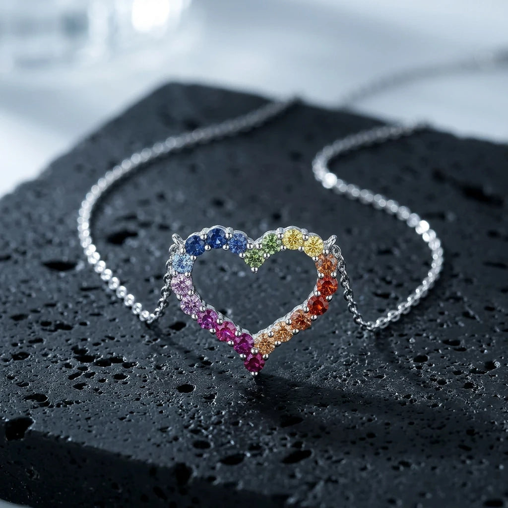 Silver 3mm round rainbow gradient open heart pendant necklace resting on textured black volcanic stone
