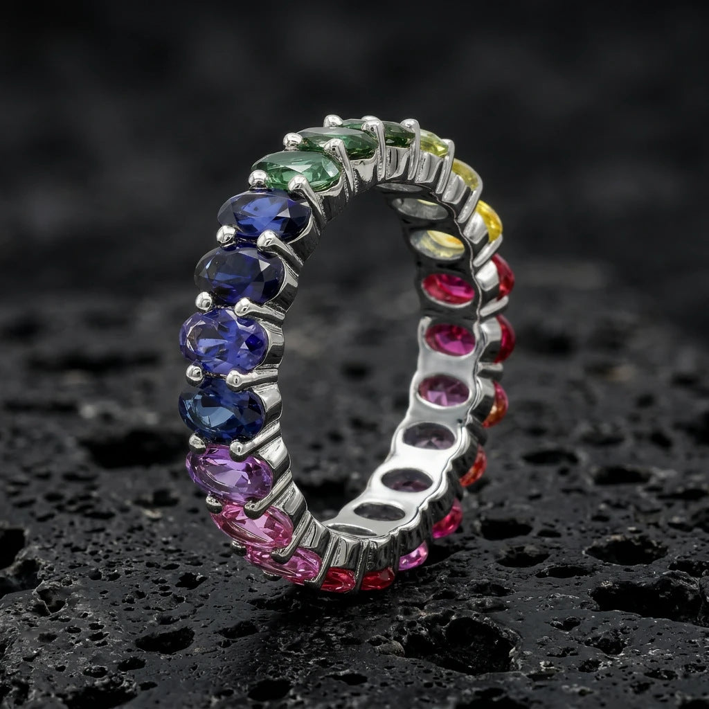Silver 3x5mm oval cut rainbow eternity band ring on textured black volcanic stone surface