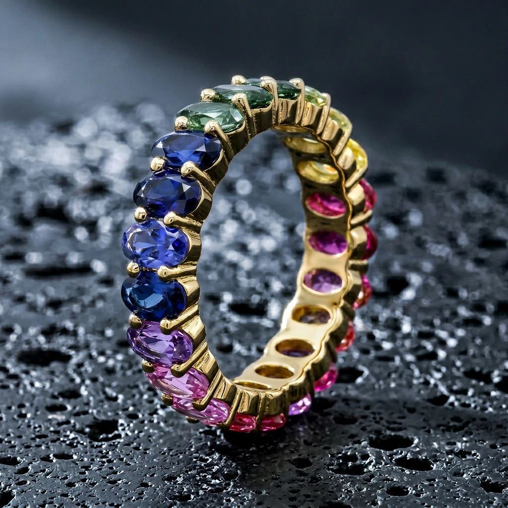 Gold 3x5mm oval cut rainbow eternity band ring on textured dark stone surface with dramatic lighting   