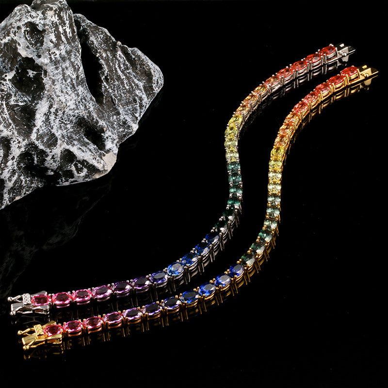 Gold and silver 4x6mm oval cut rainbow gradient moissanite tennis bracelets laid out on dark background   