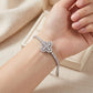 Model hand wearing 5.52 CTW diamond quatrefoil flower tennis bracelet near jewelry box.