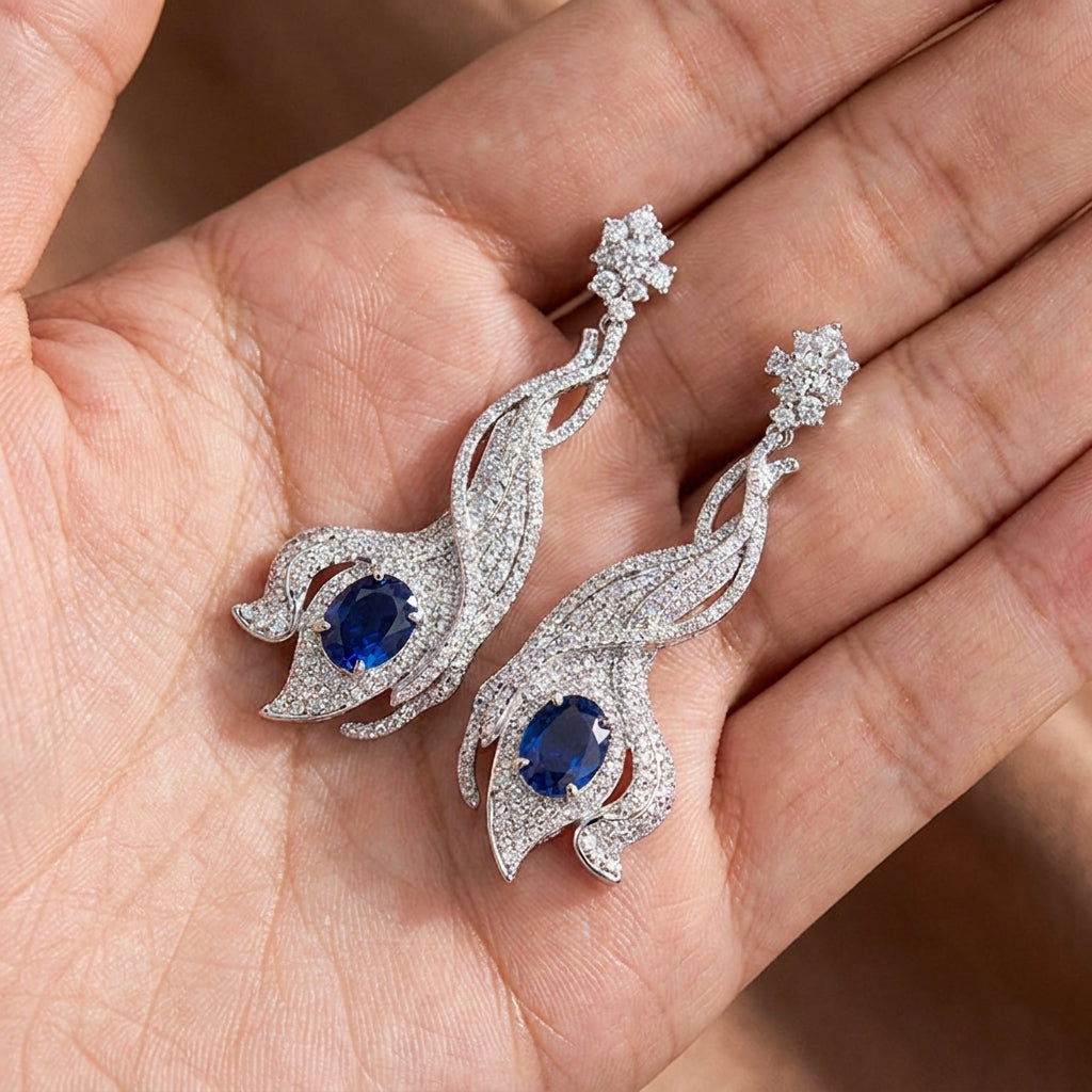 Close-up held in hand, 5ct oval-cut blue sapphire earrings, brilliant halo diamond detail.