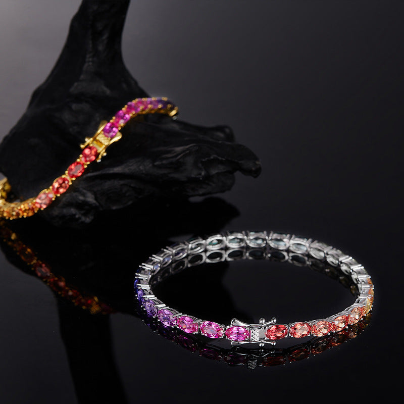 Gold and silver 5mm oval cut rainbow gradient moissanite tennis bracelets displayed on dark stone background