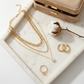 Gold jewelry including necklaces, rings, and earrings on a marble surface with a beige jewelry box.