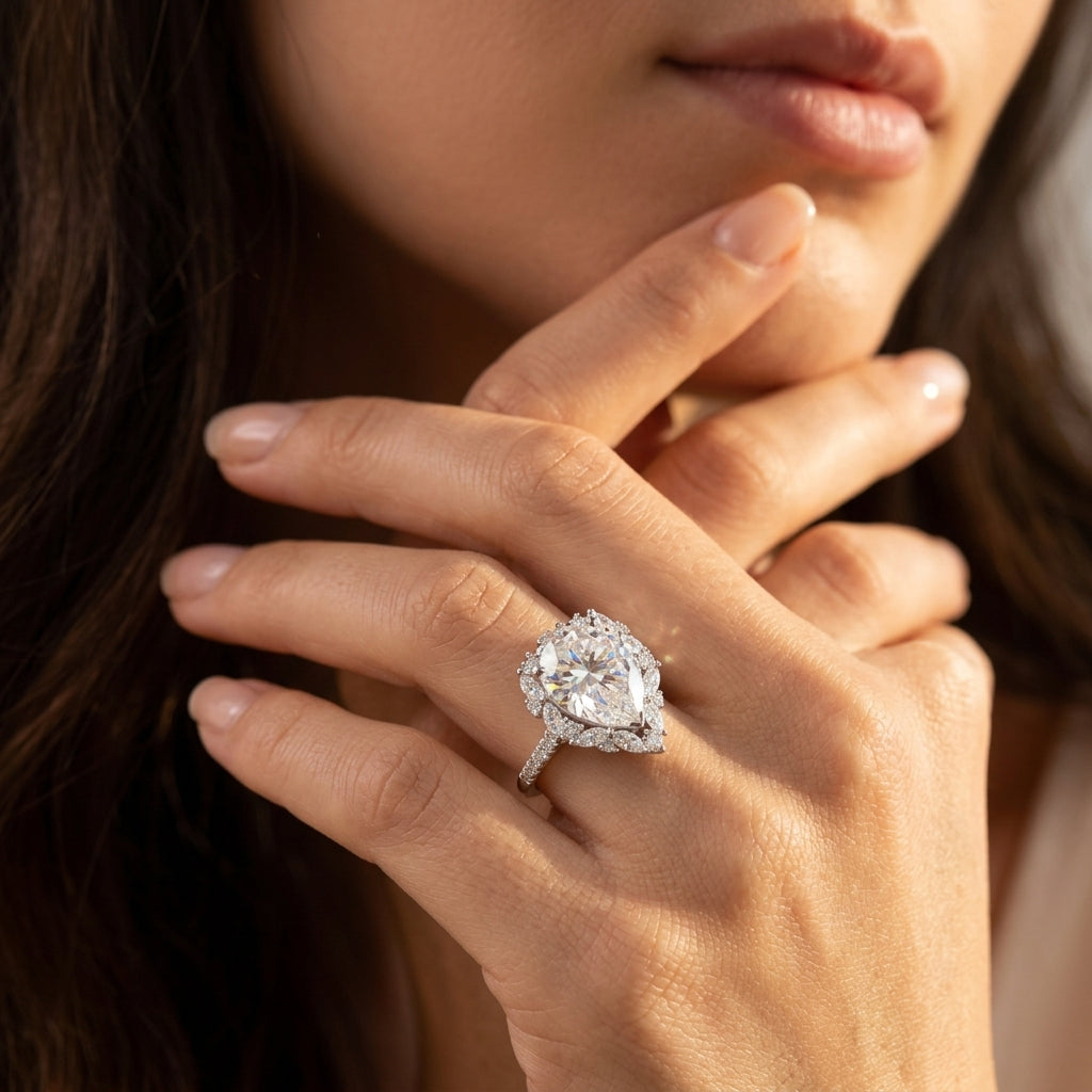 Close-up view of a model wearing an 8CT pear cut moissanite ring with marquise cluster halo.