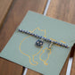 Bracelet with a cat charm on a green card with a cat illustration, placed on a wooden surface.