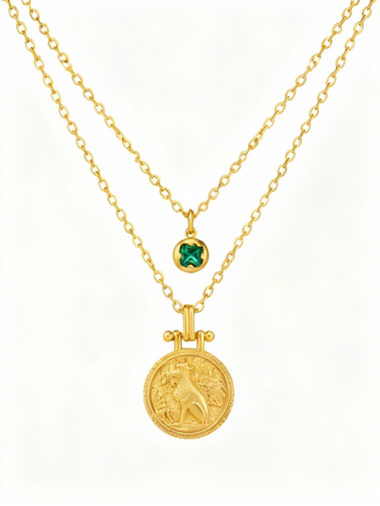 Two gold necklaces with a lion pendant and green gemstone on a white background
