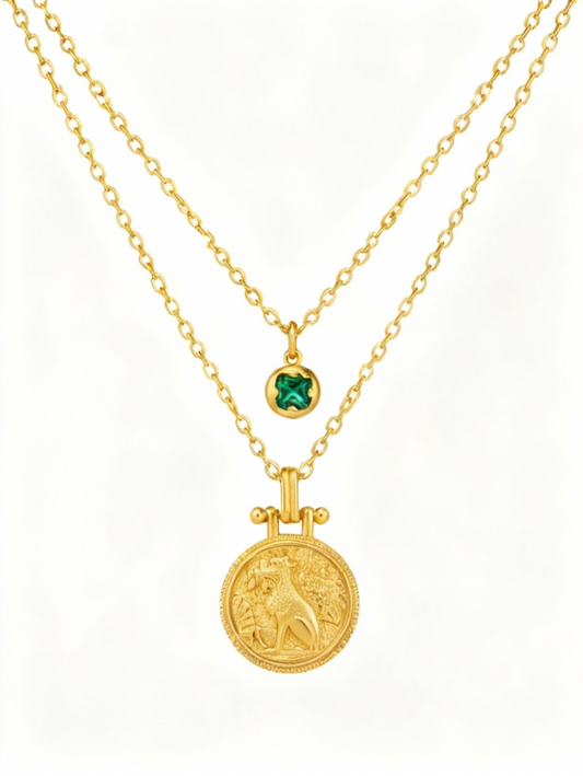 Two gold necklaces with a lion pendant and green gemstone on a white background
