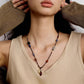 Necklace with beads worn by a person in a beige tank top, with hands holding brown fabric.