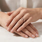 A close-up of a person's hands resting on a light marble surface, wearing two slim rose gold rings with pavé-set clear stones.