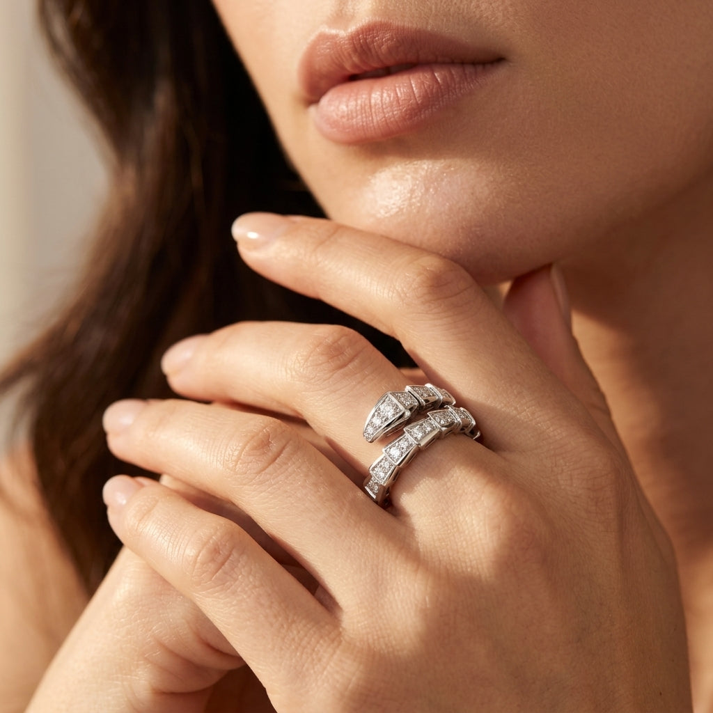 A close-up lifestyle shot of a model's hand wearing two silver rings, one featuring a row of clear pavé diamonds and the other a textured, diamond-like segmented design. The background is a soft, warm beige tone.
