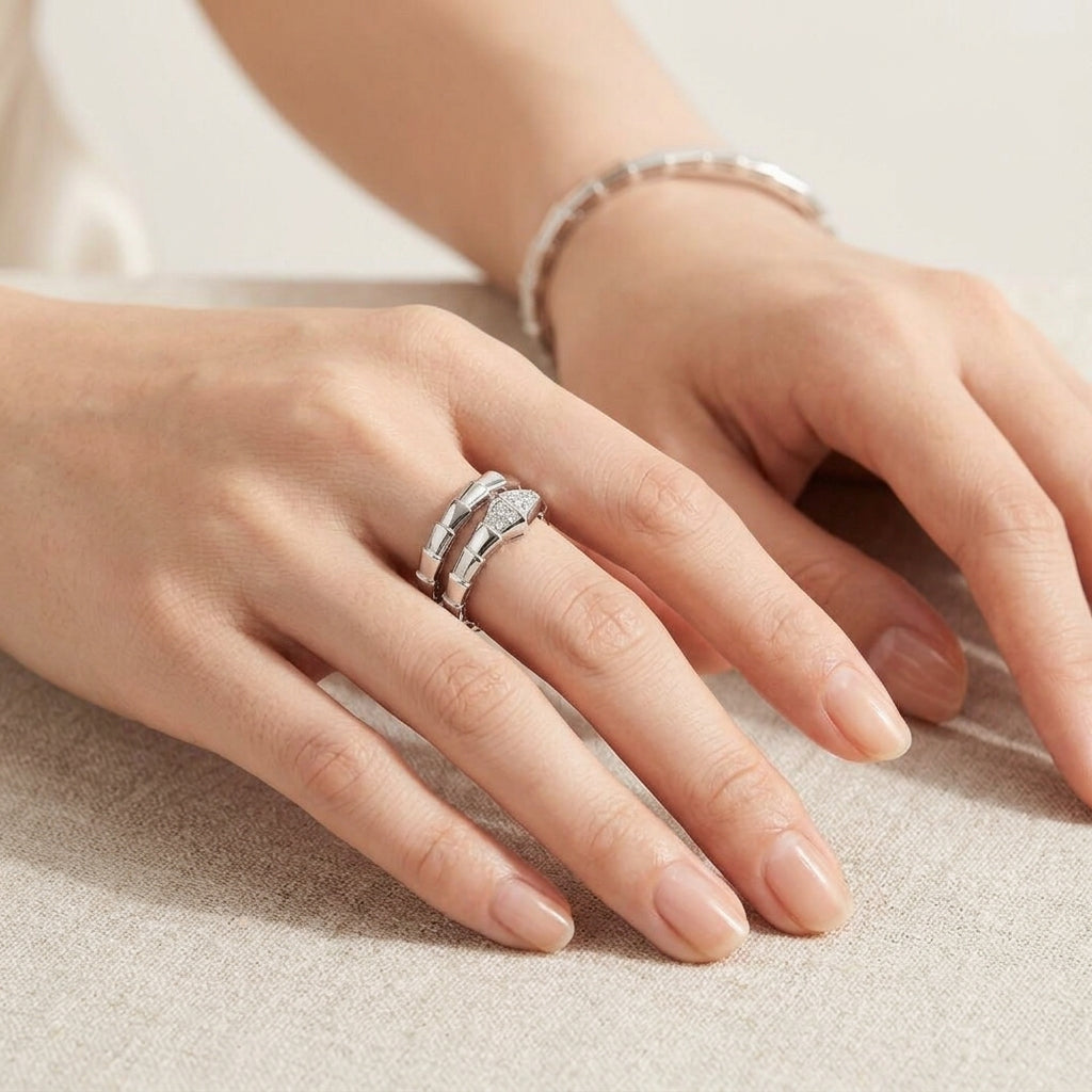 A close-up of a person's hands resting on a neutral surface, with the main focus on a silver ring featuring a curved, textured band and a matching silver bracelet on the wrist.