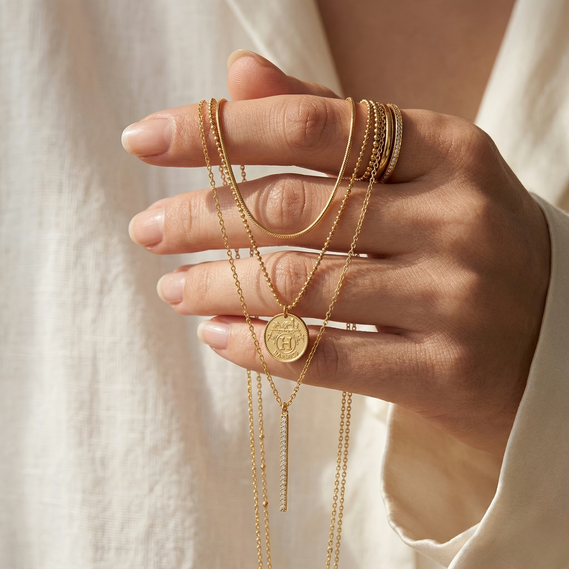 Close-up of a hand gently holding the necklace, fingers wearing matching rings, soft blurred white fabric background, natural skin texture, showing scale and intimate jewelry interaction.