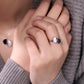 Close-up of a hand wearing a ring with a heart design, with a blurred background.