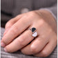 Close-up of a hand wearing a ring with a black and white stone on a gray background